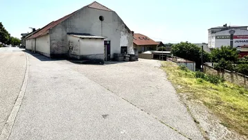Altes, verputztes Gebäude mit Satteldach und angrenzender Straße unter blauem Himmel.