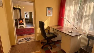 Helles Büro mit Schreibtisch und Blick auf den Kaminofen im angrenzenden Raum.