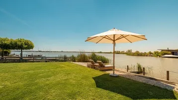 Idyllischer Gartenbereich am Seeufer mit Liegestühlen und Sonnenschirm, ideal zum Entspannen.