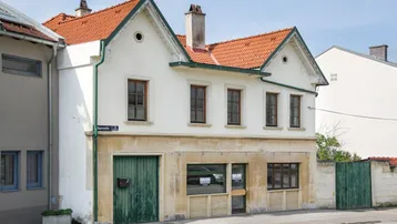 Altes Gebäude mit weißer Fassade, roten Ziegeldächern und grünen Holztüren an der Straße.