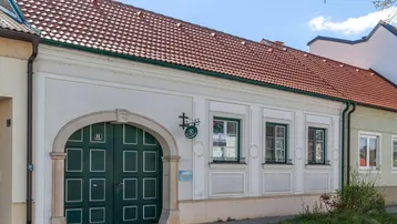 Traditionelles Gebäude mit großem Holztor und roten Ziegeldächern in ländlicher Umgebung.