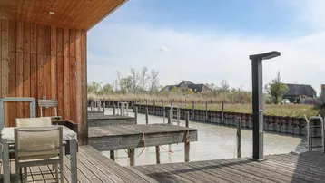 Große Holzterrasse mit Sitzgelegenheiten und direktem Zugang zu Bootsanlegestellen am Kanal.
