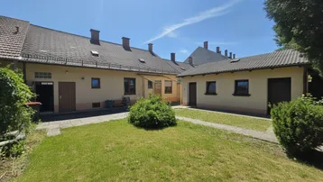 Innenhof mit Rasenfläche und Gebäudefassade unter blauem Himmel an einem sonnigen Tag.