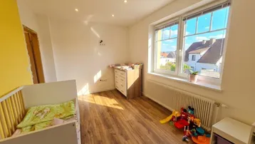 Helles Kinderzimmer mit Babybett, Wickelkommode, Spielzeug und Blick ins Grüne.
