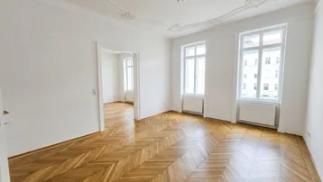 Helles Wohnzimmer mit Fischgrätparkett, hohen Decken und dekorativen Stuckelementen.