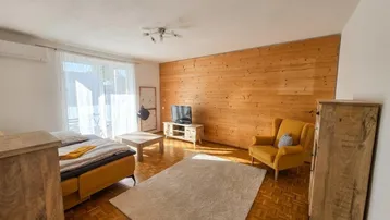 Helles Wohnzimmer mit Holzwand, Parkettboden und Zugang zu einem Balkon.