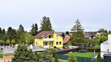 Blick von oben auf ein gelbes Einfamilienhaus mit großem Garten und Trampolin, umgeben von Bäumen.