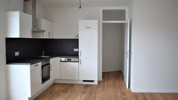 Moderne Küche mit weißen Schränken, dunkler Arbeitsplatte und Holzboden in einem offenen Wohnbereich.