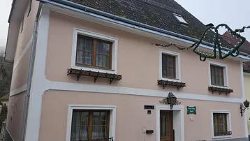 Traditionelles Wohnhaus mit rosafarbener Fassade, Satteldach und Holzfenstern an einer ruhigen Straße.