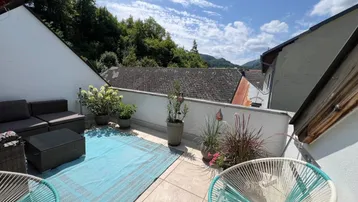Sonnige Dachterrasse mit modernen Gartenmöbeln, blauem Teppich und Pflanzen, bietet einen weiten Blick.