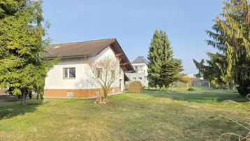 Großzügiger Gartenbereich mit Rasenfläche und Nadelbäumen, umgeben von einer ländlichen Umgebung.