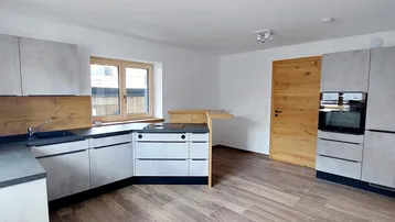 Moderne Küche mit grauen Fronten, Holzakzenten, integrierten Geräten und einem kleinen Frühstücksbereich.