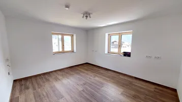 Heller, leerer Raum mit Holzfenstern und modernem Fliesenboden in Holzoptik.