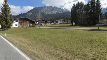 Blick auf traditionelle Häuser in einer ländlichen Umgebung mit grünen Wiesen und schneebedeckten Bergen im Hintergrund.