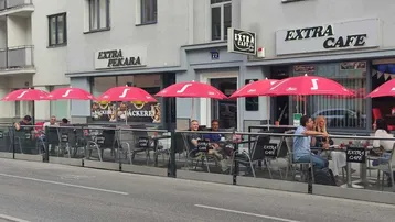 Straßencafé mit roten Sonnenschirmen und Glasabtrennung, belebt mit Gästen.