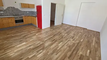 Heller offener Wohnbereich mit integrierter Küche, Holzfußboden und einem auffälligen roten Kühlschrank.