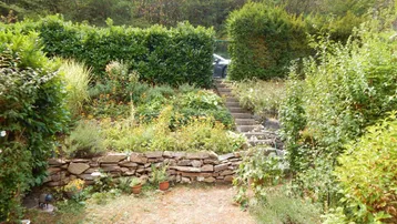 Stufenförmiger Garten mit Steinmauern und üppiger Vegetation, der zum Entspannen einlädt.