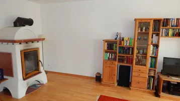 Gemütliches Wohnzimmer mit traditionellem Kachelofen, Holzregalen und Parkettboden.