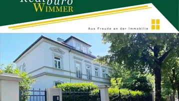 Elegante Villa mit klassischer Architektur und einem Immobilienmakler-Logo im oberen Bereich.