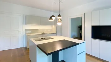 Moderne Küche mit Kücheninsel, integriertem Kochfeld und hellen Schränken.
