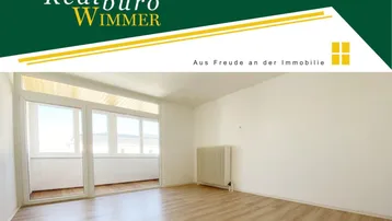 Heller, leerer Wohnraum mit großen Fenstern, Laminatboden und Zugang zu einem Balkon.