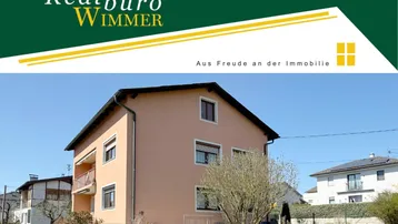 Ansicht des Wohnhauses mit gepflegtem Vorgarten und Werbebanner des Immobilienbüros.