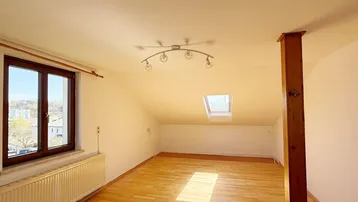 Lichtdurchfluteter Dachgeschossraum mit Parkettboden, Dachfenster und weitem Blick.