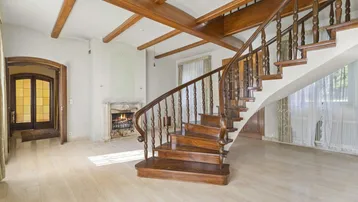 Beeindruckender Eingangsbereich mit geschwungener Holztreppe, Kamin und Marmorboden.