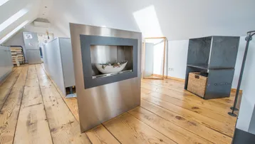 Heller Dachbodenbereich mit Holzdielenboden und einem modernen Kamin als Blickfang.