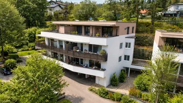 Moderne Wohnanlage mit mehreren Balkonen und Dachterrasse, eingebettet in eine grüne Umgebung.