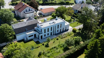Moderne Villa mit Flachdach und großem Garten, umgeben von weiteren Wohnhäusern in grüner Umgebung.