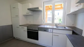 Funktionale Küche mit weißen Fronten, Spülmaschine und Blick ins Grüne durch das Fenster.