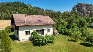 Haus mit Garten und Bergblick unter blauem Himmel in ländlicher Umgebung.
