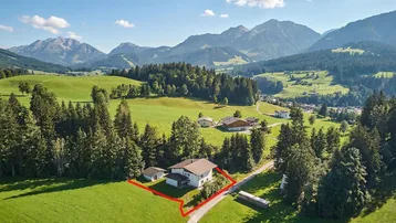 Luftaufnahme eines Hauses in einer grünen Berglandschaft mit klar abgegrenztem Grundstück.