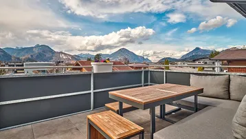 Große Dachterrasse mit modernen Gartenmöbeln und atemberaubendem Panoramablick auf die umliegenden Berge.
