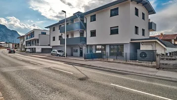 Moderne Wohnanlage mit Balkonen, großen Fenstern und Bergblick unter bewölktem Himmel.