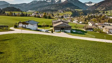 Luftaufnahme einer ländlichen Siedlung mit Häusern und beeindruckendem Bergpanorama unter blauem Himmel.