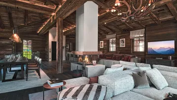 Geräumiger, offener Wohn- und Essbereich im Chalet-Stil mit Holzbalken, Kamin und gemütlicher Sitzecke.