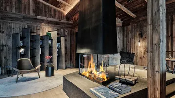 Gemütliches Wohnzimmer im Chalet-Stil mit modernem Kamin als Mittelpunkt und Holzbalkendecke.