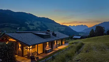 Modernes Chalet in alpiner Landschaft bei Sonnenuntergang mit beleuchteter Terrasse.