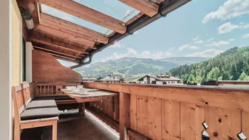 Gemütlicher Holzbalkon mit Glasdach, Sitzbank und herrlichem Bergblick lädt zum Verweilen ein.