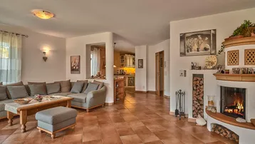 Gemütliches Wohnzimmer mit traditionellem Kachelofen, bequemer Sofalandschaft und Terrakotta-Fliesenboden.