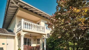 Außenansicht des Hauses mit überdachter Terrasse, Balkon und gepflegtem Gartenbereich.
