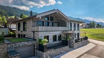 Modernes Chalet mit Holzfassade, Steinelementen und Bergblick unter blauem Himmel.