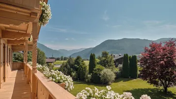 Geräumiger Holzbalkon mit Blumenkästen und weitem Blick über das grüne Tal und die Berge.