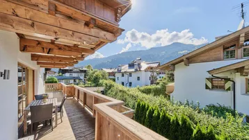 Sonniger Balkon mit Holzboden, Sitzgelegenheiten und malerischem Bergblick auf die Alpen.