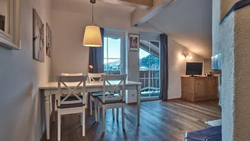 Heller Essbereich mit Holztisch und Stühlen, Balkonzugang und einem schönen Bergblick.