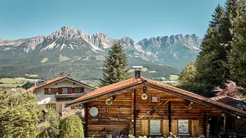 Rustikales Holzhaus mit traditioneller Architektur und beeindruckendem Bergblick unter blauem Himmel.