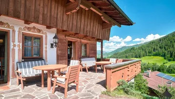 Geräumige Sonnenterrasse mit traditionellen Holzmöbeln und weitem Blick auf die umliegende Berglandschaft.