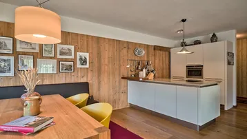 Offener Wohn- und Essbereich mit moderner Küche, Holzvertäfelung und Holzboden.